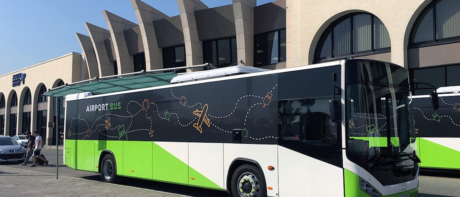 Un autobús Airport Bus verde y blanco parado delante de la fachada de la terminal del aeropuerto de Malta