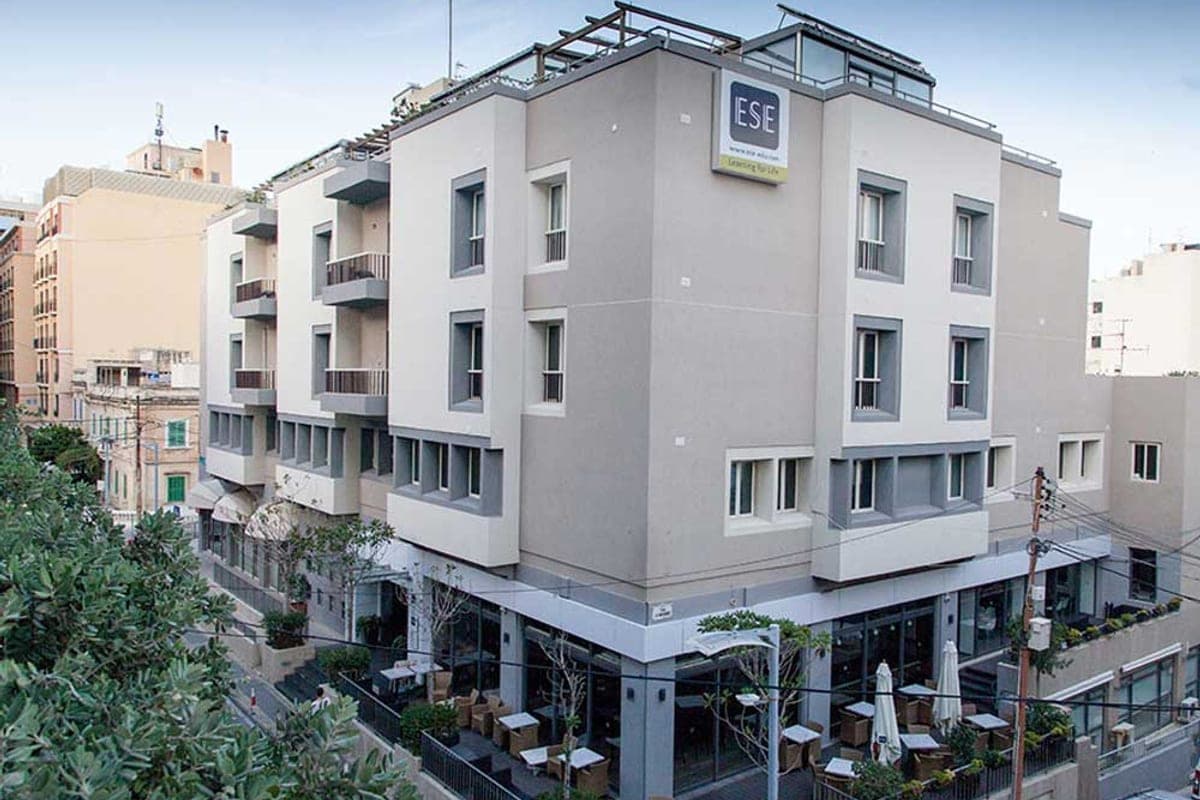 El edificio de ESE en Paceville, St Julian's: fachada clara de cinco plantas con el rótulo de la escuela y la terraza de la cafetería a pie de calle