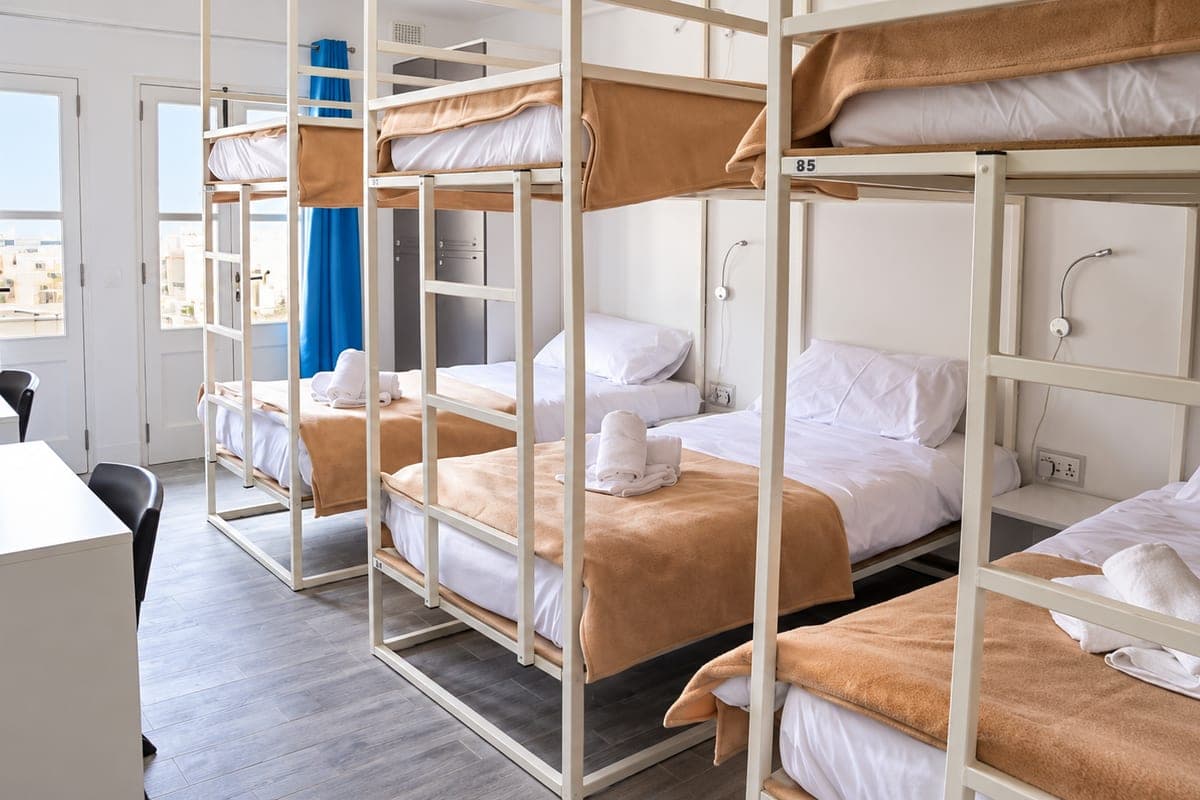 Una habitación con literas de estructura blanca, camas hechas con mantas marrones y ventana con luz