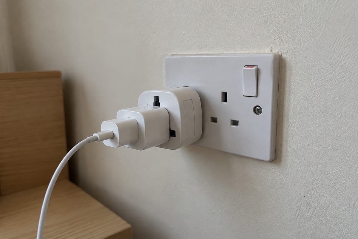 Primer plano de un enchufe de pared británico tipo G en una habitación de hotel de Malta, con un adaptador europeo enchufado y un cargador de móvil