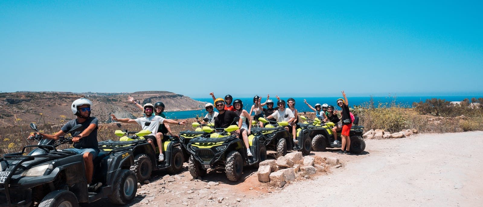 Un grupo de una excursión en quad en lo alto de una pista de tierra de Gozo, con los quads en fila, los cascos puestos y el mar al fondo