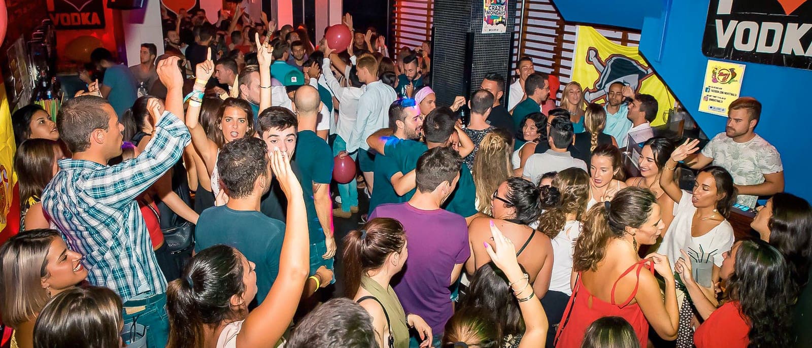 Un local de Paceville lleno de gente joven bailando en la Spanish Party, luces de colores y los brazos en alto