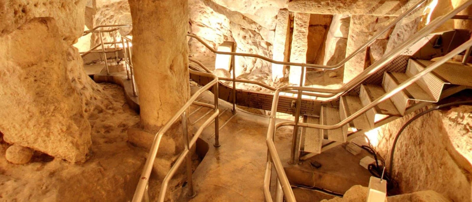 El interior del Hipogeo: las salas talladas en la roca del nivel medio con las pasarelas y escaleras metálicas de la visita, luz cálida