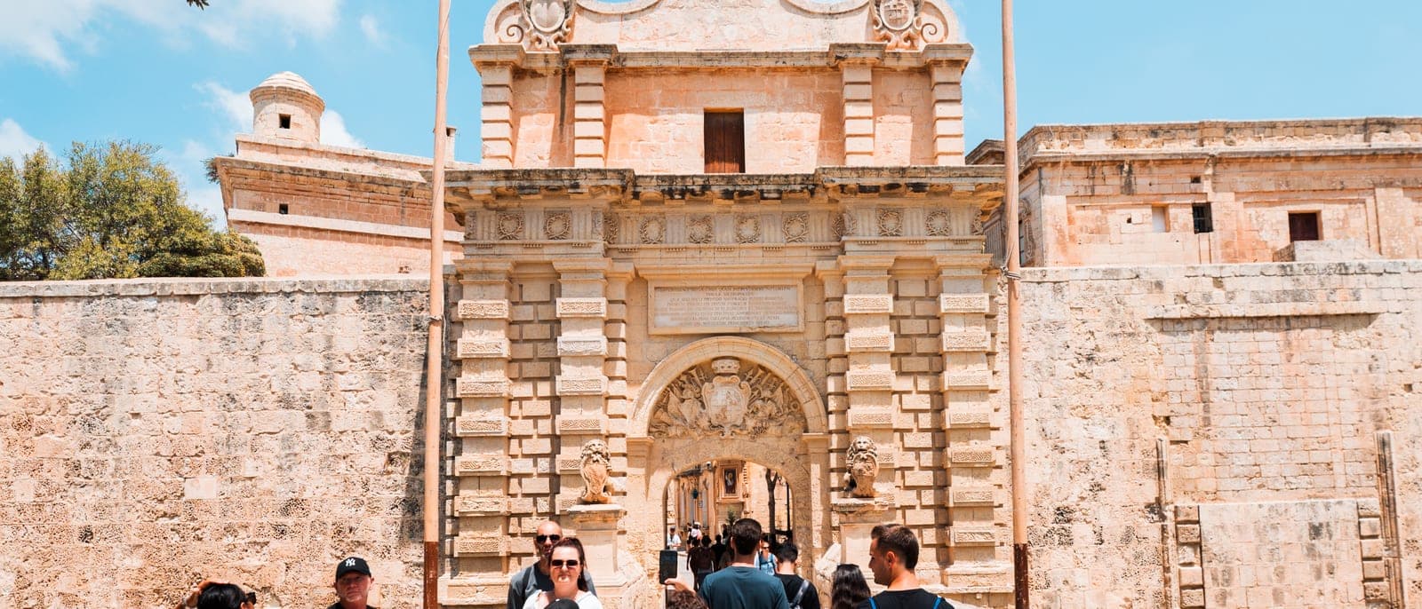 La puerta principal de Mdina vista desde el puente sobre el foso, con la muralla dorada y visitantes cruzando hacia la ciudad