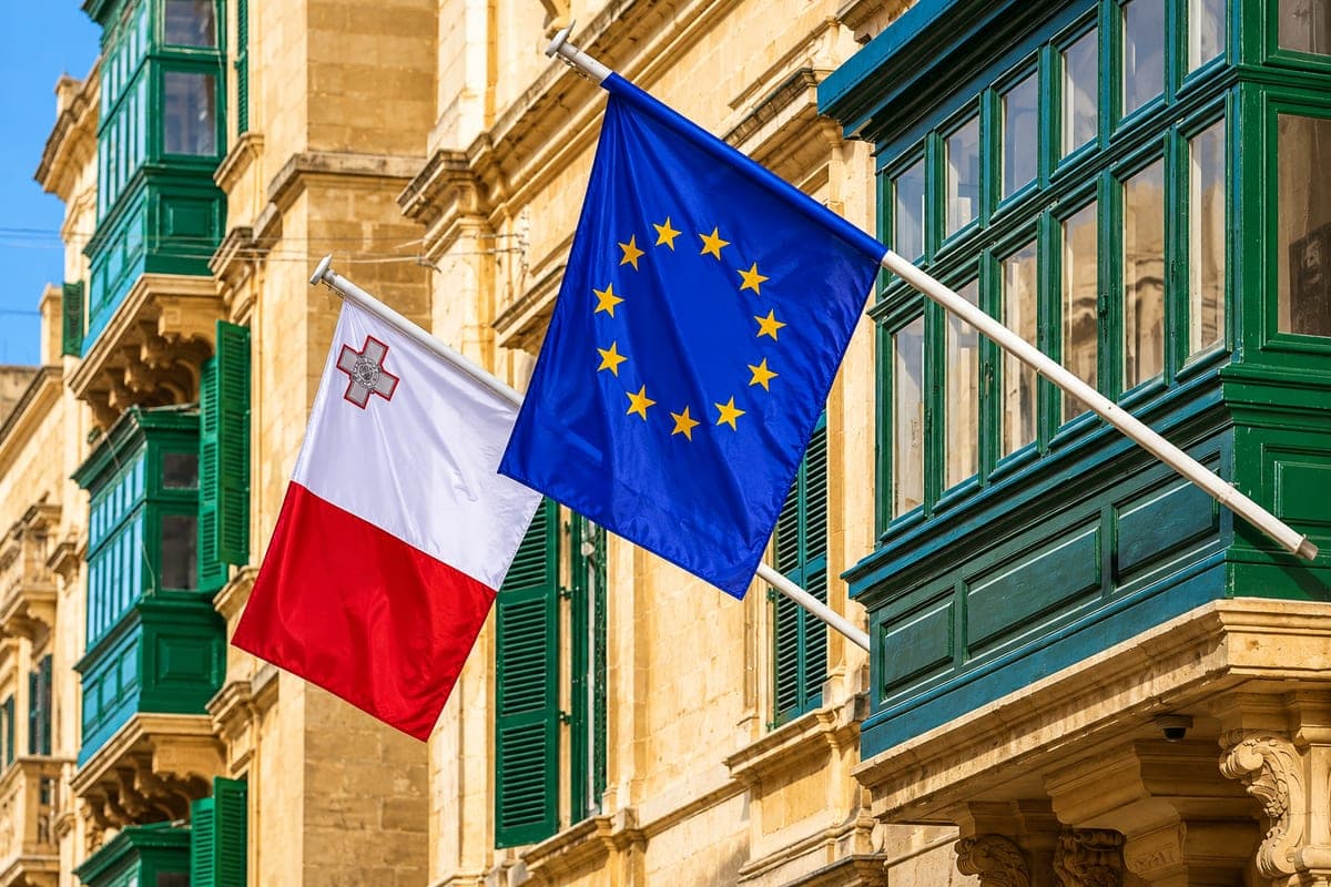 Las banderas de Malta y de la Unión Europea ondeando juntas en una fachada de piedra dorada de La Valeta, entre los balcones de madera verdes