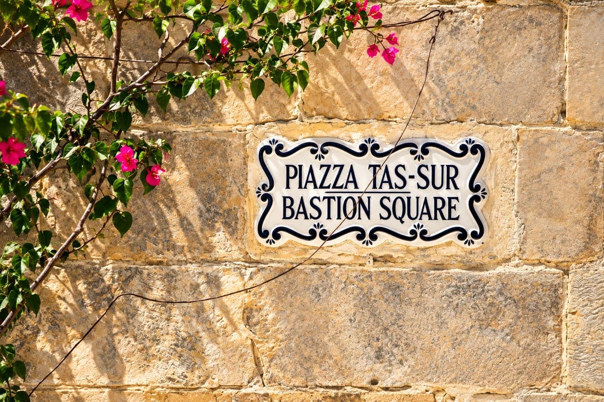 El cartel de azulejo de la plaza del Bastión de Mdina, Piazza Tas-Sur y Bastion Square, en maltés y en inglés, en un muro de piedra con una buganvilla