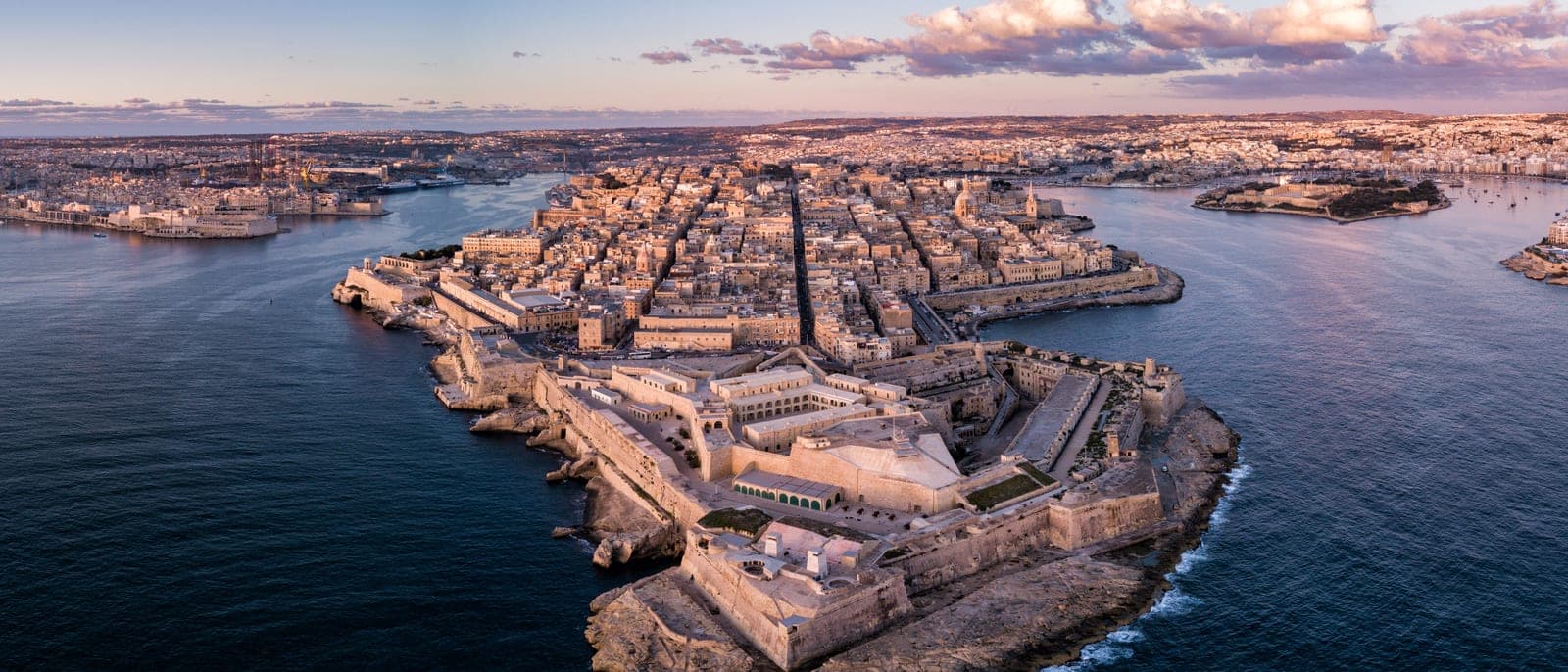 La península de La Valeta desde el aire al atardecer, con el Grand Harbour a un lado, Marsamxett al otro y la densidad de piedra y bastiones