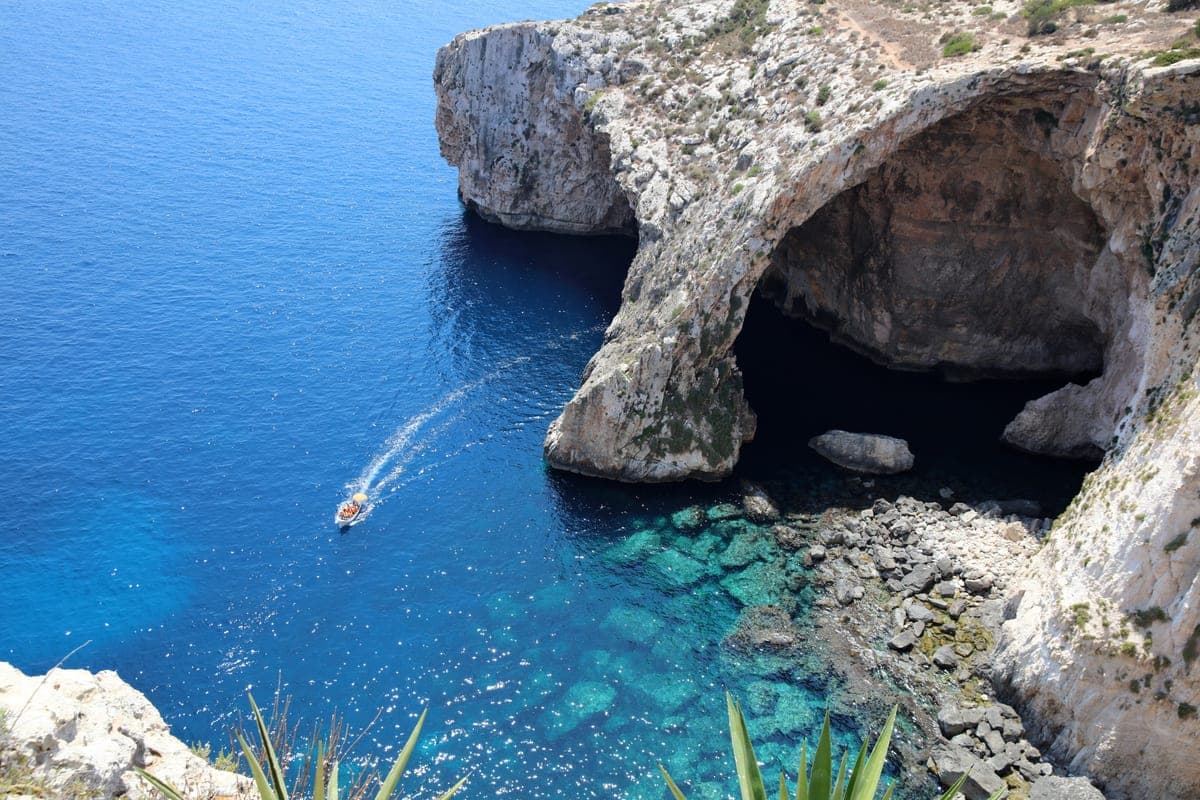 El arco de la Gruta Azul visto desde arriba, con una lancha entrando por debajo y el agua azul y transparente sobre las rocas