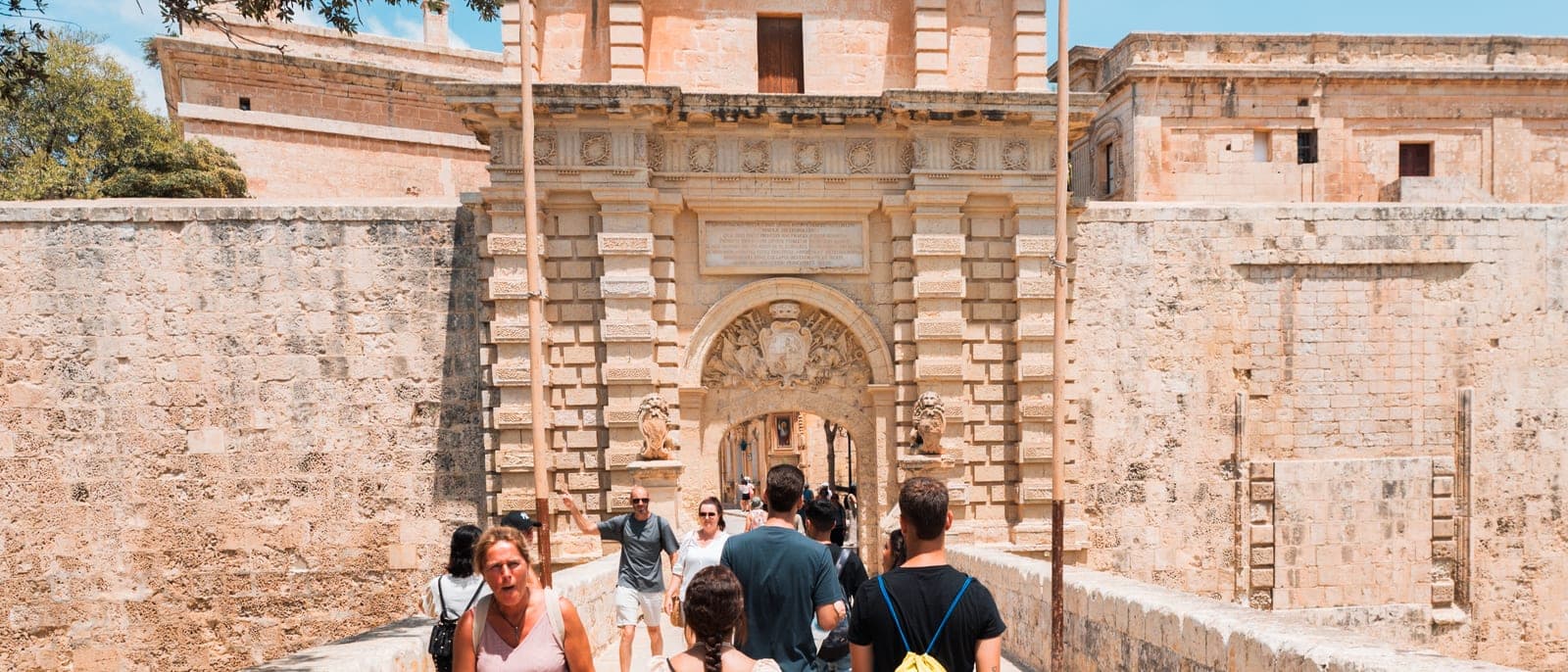 La puerta principal de Mdina y su muralla dorada vistas desde el puente sobre el foso, con visitantes entrando