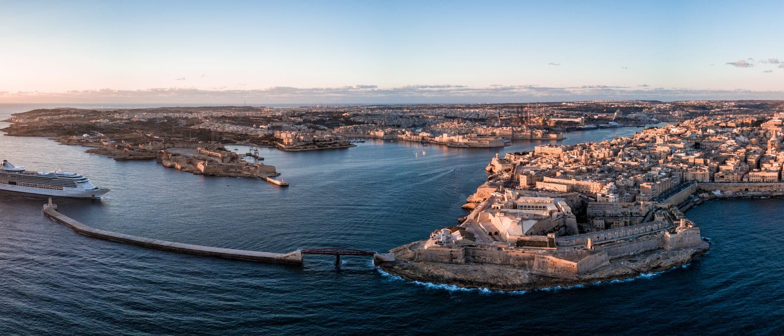 El Grand Harbour de La Valeta desde el aire al atardecer: la ciudad amurallada en su península, las Tres Ciudades enfrente, un crucero atracado y el mar en calma