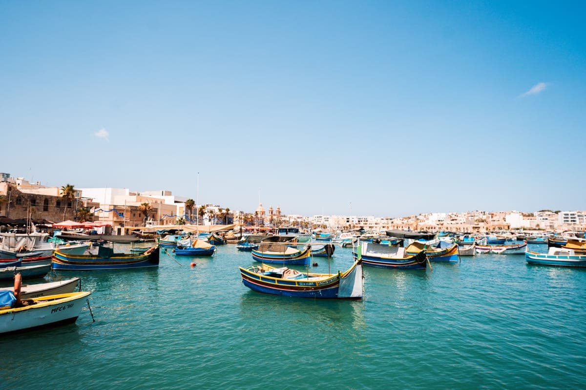 Barcas de pesca luzzu de colores amarradas en el puerto de Marsaxlokk, con el ojo pintado en la proa, y el pueblo al fondo