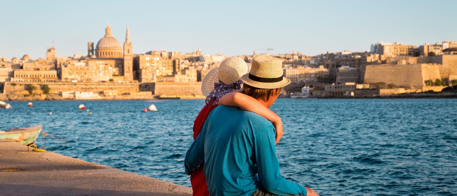 Una pareja sentada en el paseo de Sliema mirando La Valeta al otro lado del puerto de Marsamxett, a última hora de la tarde