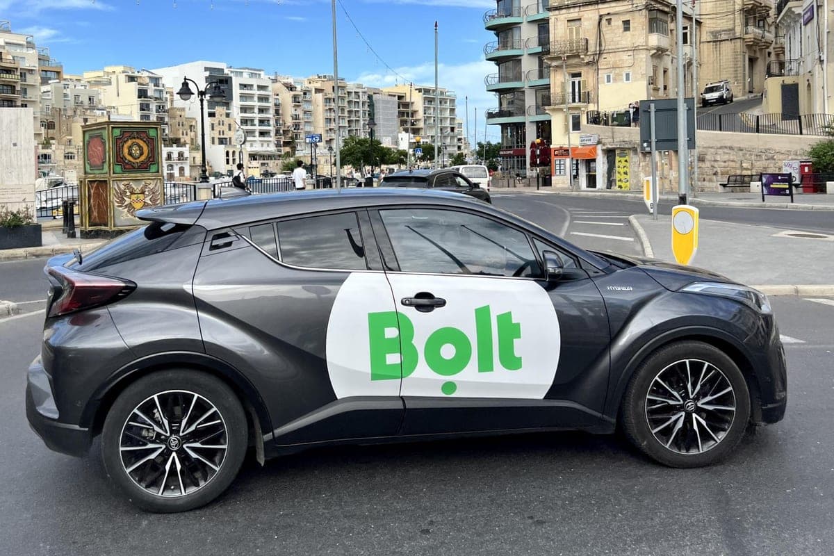 Un coche con el rótulo de Bolt parado en una calle de St Julian's, con los edificios y la bahía detrás