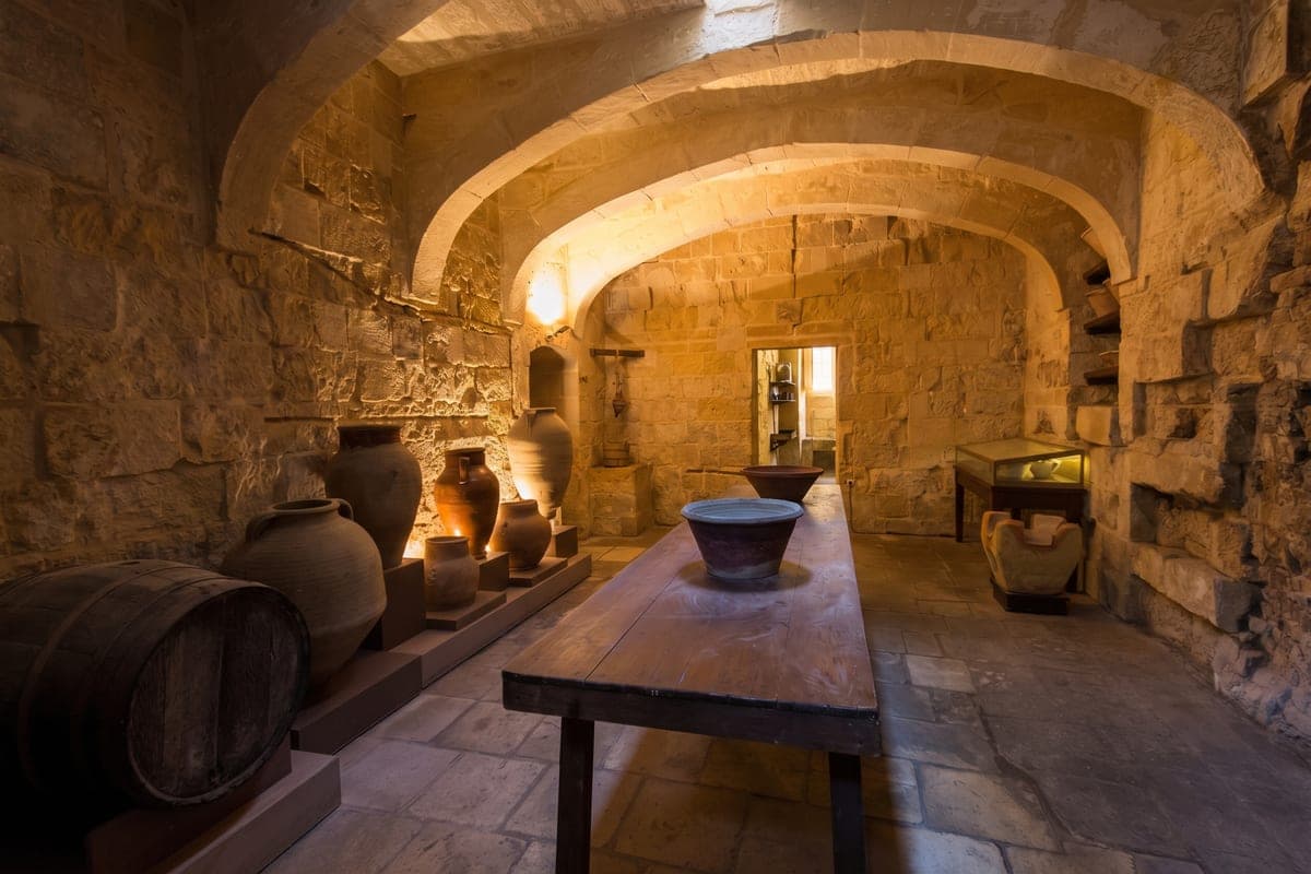 La cocina del Palacio del Inquisidor en Birgu: bóvedas de piedra, una mesa larga de madera, tinajas de barro y un barril