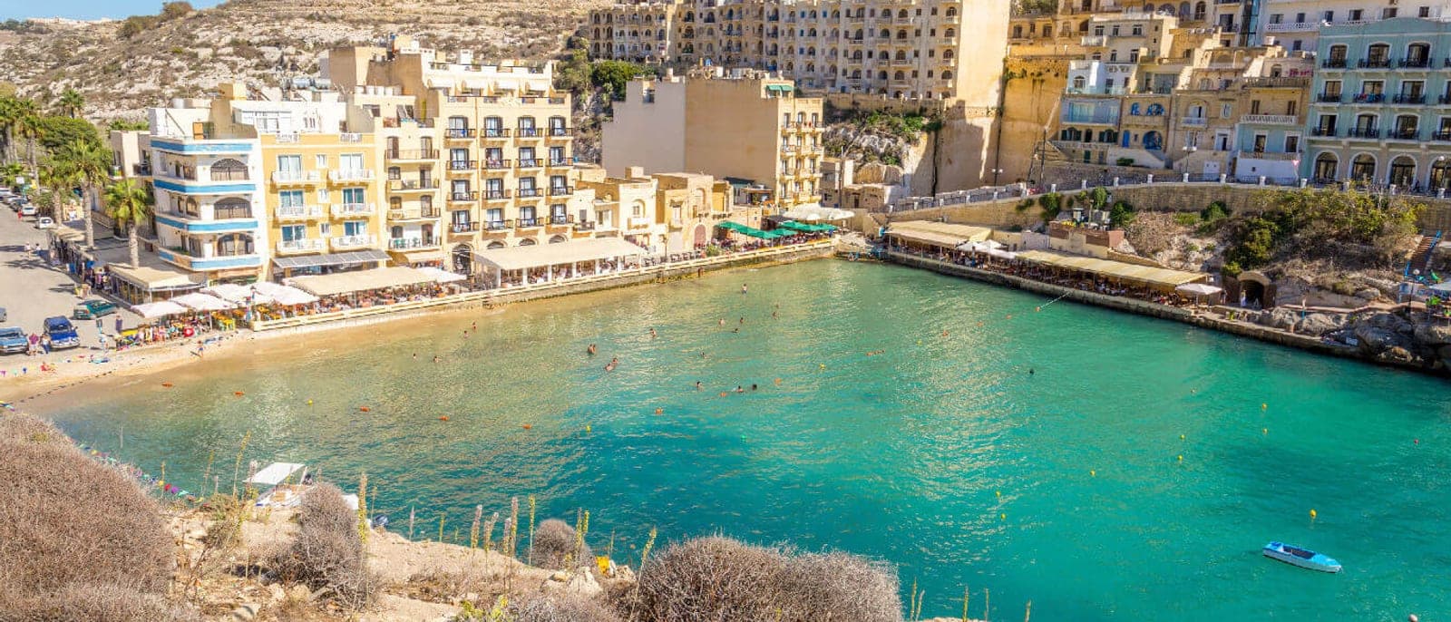 La cala de Xlendi vista desde el camino del acantilado: la bahía estrecha entre paredes de roca, los hoteles y las terrazas al borde del agua